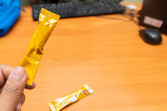 Hispanic hand holdig a yellow blank cooffee sashet  in a offices with a pc at bachgrounds.