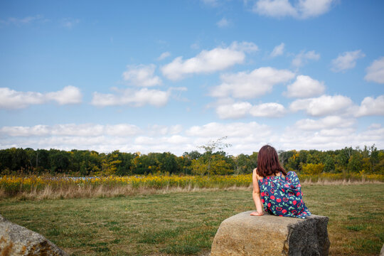 A little girl sits by self on large rock looking out at prairie