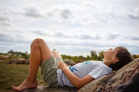 A young boy lays back on rock barefoot in sunshine