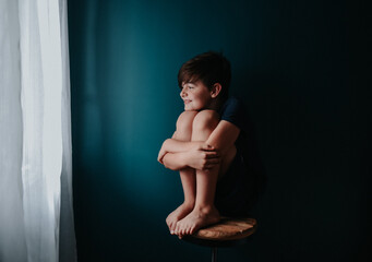 Happy young boy sitting on a stool against a dark blue wall.