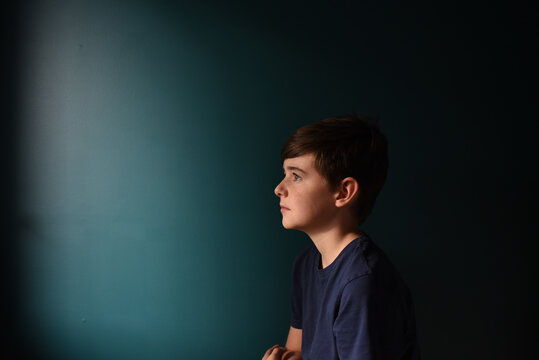 Portrait of a sad young boy against a dark blue wall.