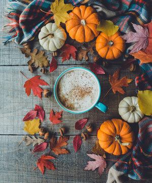 Overhead of pumpkin spice latte on wood with leaves and pumpkins.