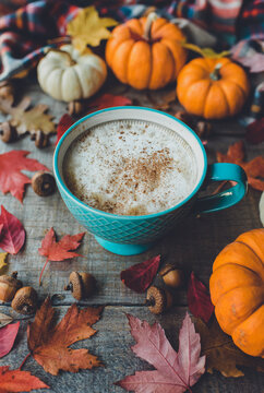 Pumpkin spice latte on wooden table with leaves and pumpkins.