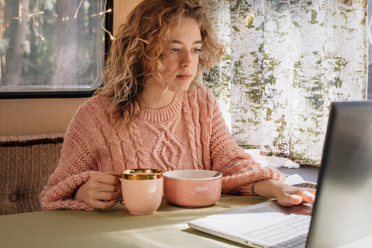 Woman in trailer eating breakfast at laptop.