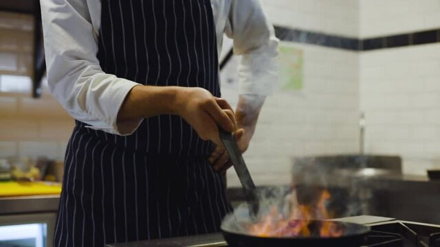 Slow motion of chef cooking with fire provokes flames in pan in a professional kitchen