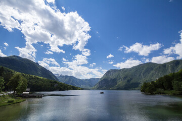Panorama of Lake Bohinj, also called bohinjsko jezero, on a sunny afternoon, with a boat crusing on the waters. Bohinj lake is a major landmark of the Julian Alps mountain chain in Slovenia, Europe.