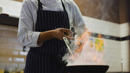 Slow motion track right and then up of chef cooking with fire in pan in a professional kitchen - Powered by Adobe