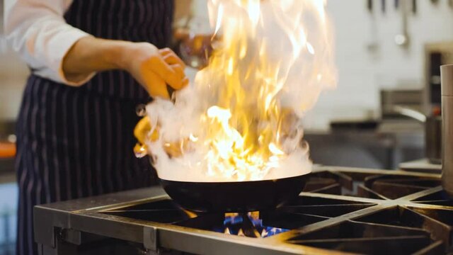 Slow motion chef sets pan on fire in professional kitchen close up on pan