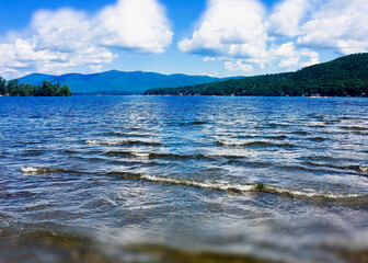 lake water lapping beach and mountains with bright clouds