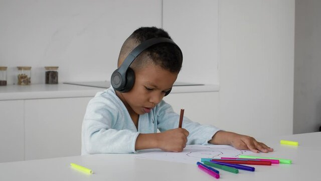 Little Black Boy Wearing Wireless Headphones Drawing With Colorful Pencils At Home