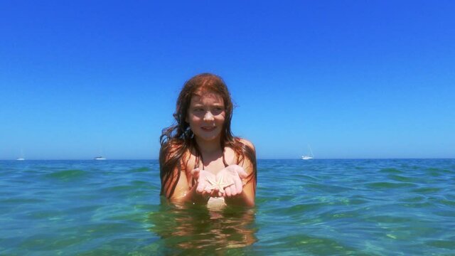 Beautiful adorable red hair child girl bathing in sea water hold starfish in hands. Slow-motion