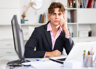 Upset attractive young businessman working documents and laptop in modern office