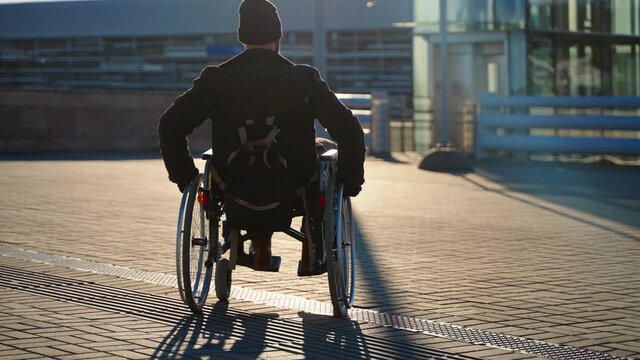 wheelchair-bound man is walking alone on city street, moving to lift for disabled people