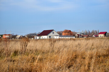 The picture shows a field overgrown with dry grass and houses on the horizon.