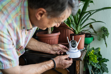 Caucasian senior man holding home security surveillance camera and mobile phone trying to install...