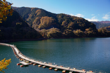 Floating bridge made of drum containers in a blue lake in Okutama, Japan, sunny autumn day