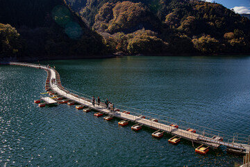 Fototapeta na wymiar Floating bridge made of drum containers in a blue lake in Okutama, Japan, sunny autumn day