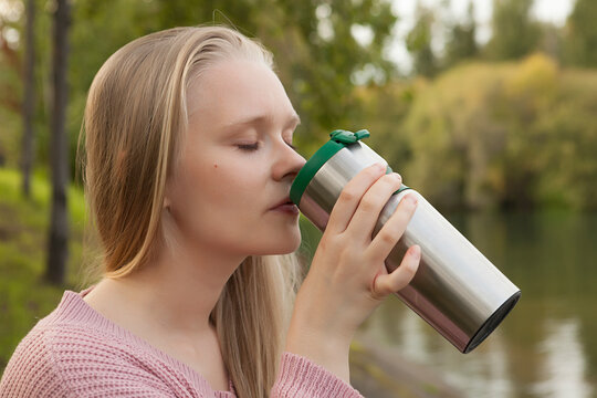 young girl in nature drinks from a thermos, a thermos with a hot drink, a blonde girl on a walk