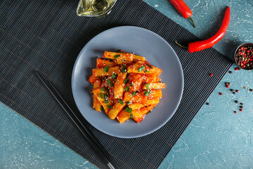 Plate with honey chilli potato and chopsticks on color background