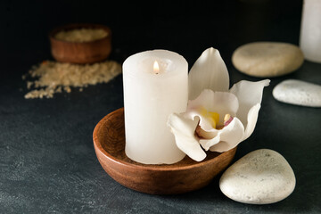 Bowl with flower and burning candle on dark background