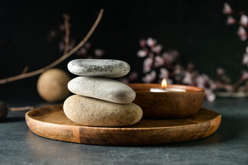 Fototapeta na wymiar Wooden tray with stack of spa stones on dark background