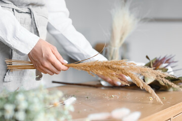 Female florist making bouquet with beautiful dried flowers at table, closeup