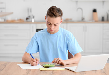 Teenage boy using calculator at table in kitchen