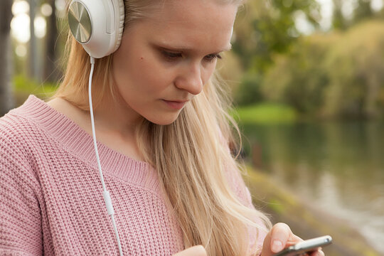  young girl in white headphones listening to music, young girl with a smartphone in her hands walking with headphones, listening to music
