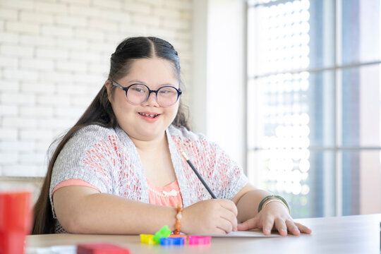 Portrait of cute little down syndrome girl writing on the table at home