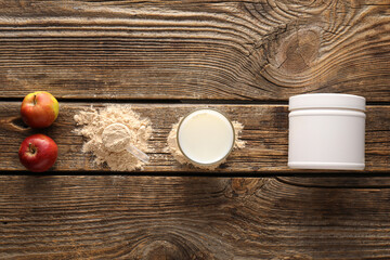 Glass of protein shake, powder, apples and jar on wooden background