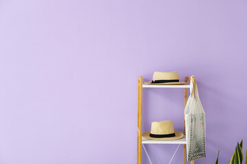Shelving unit with straw hats and bag near lilac wall