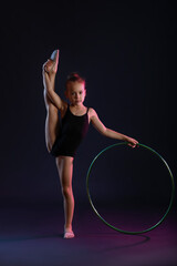 Little girl doing gymnastics  with hula hoop on dark background