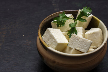 A bowl full of cubes of organic juicy cottage cheese or paneer with dark background. Selective focus.
