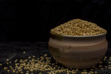 A bowl full of organic Mung dal or lintel with dark background. Selective focus.