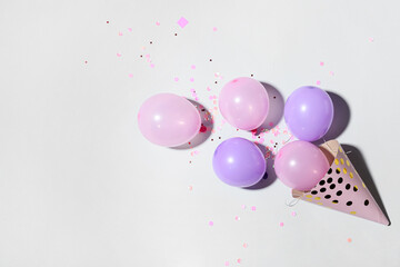 Party hat with beautiful balloons and confetti on light background