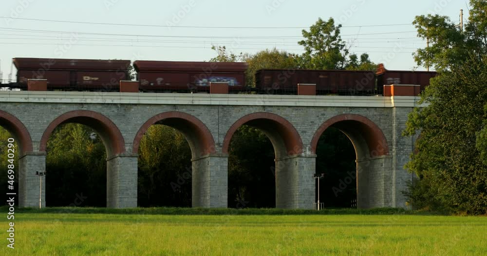Poster a railway viaduct in the middle of a field with a freight train passing through it.