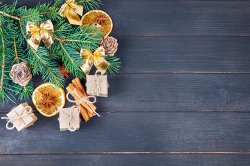 christmas decorations, Christmas tree branches, gift boxes, a slice of dried orange and a stick of cinnamon on a wooden background close-up view from above