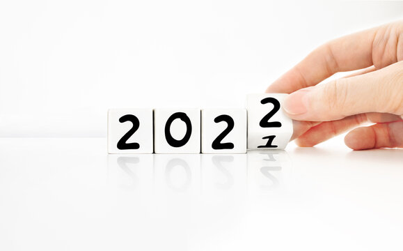 Person's hand holding white cube turning from the year 2021 to 2022 with a reflection on white background. A minimal concept with copy space. Goodbye to the past, welcome to the coming new year.