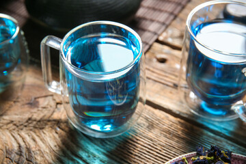 Glass cups of organic blue tea on wooden background, closeup
