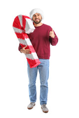 Handsome man in Santa hat with candy cane pinata showing thumb-up on white background
