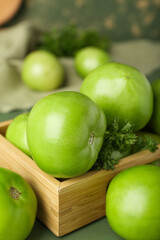 Wooden box with fresh green tomatoes on table, closeup