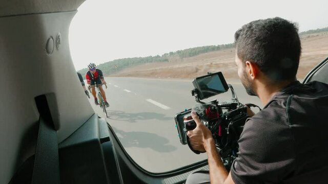 a professional videographer filming two road bikers on the road from the back trunk of a car while they drive