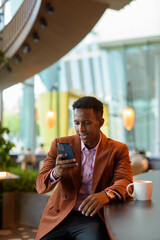 African businessman sitting in coffee shop using phone