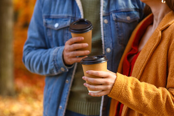 Young couple holding paper cups with drink in autumn park, closeup