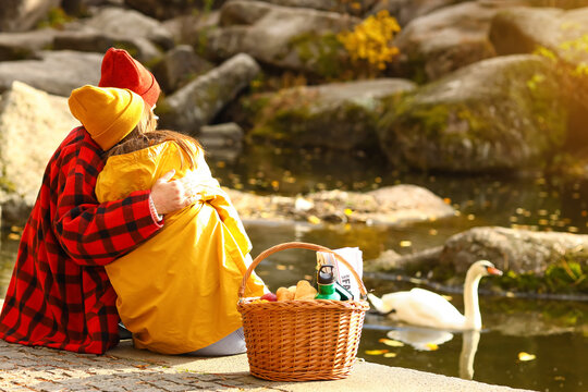 Loving couple with picnic basket sitting near pond in beautiful autumn park