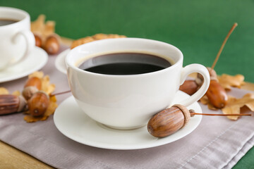 Board with cup of coffee and acorns on table, closeup