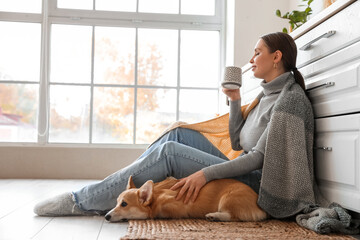 Young woman with cute Corgi dog and cup of tea in kitchen