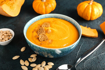 Bowl with delicious pumpkin cream soup and seeds on dark background