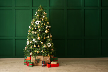 Beautiful Christmas tree with gifts near green wall