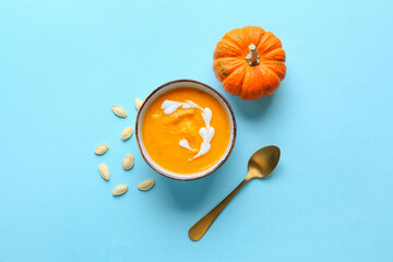 Bowl with delicious pumpkin cream soup and seeds on blue background